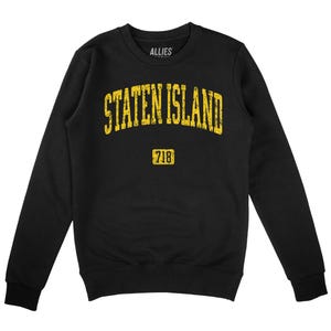 Könnte beinhalten: Schwarzes Sweatshirt mit Rundhalsausschnitt und dem Text "STATEN ISLAND" in vergilbter gelber Schrift. Darunter die Nummer "718" in einem gelben Rechteck. Der Markenname "ALLIES" steht darüber.