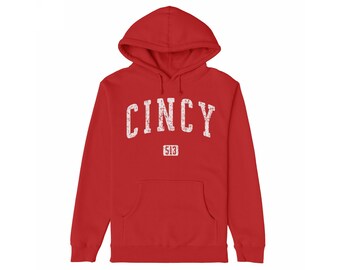 May include: A red hoodie featuring the word "CINCY" in distressed white lettering. Below the word "CINCY" is the number "513" in a white rectangle. The sweatshirt has a front pocket and a drawstring hood.