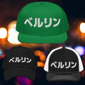 Op de afbeelding: Drie baseballpetten met het Japanse woord "ベルリン" (Berlijn) in wit geborduurd op de voorkant. De petten zijn groen, zwart en zwart met een wit mesh achterkant.