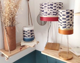 May include: Three hanging lamps with white fabric shades and geometric patterns in black and white. The lamps are suspended from rope and have different sized shades. The lamps are on wooden shelves against a teal wall.