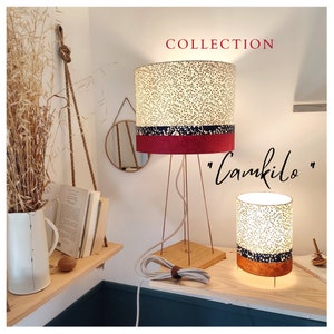 May include: Two table lamps with cylindrical shades featuring a cream leaf pattern, a dark blue band, and a solid base. The taller lamp has a wooden square base and thin copper legs. The text "COLLECTION" and "Camkilo" appear in the image.