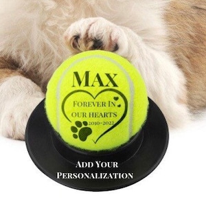 May include: A yellow tennis ball with a black heart and paw print design. The ball is personalized with the name "MAX" and the text "Forever in our hearts 2010-2022".
