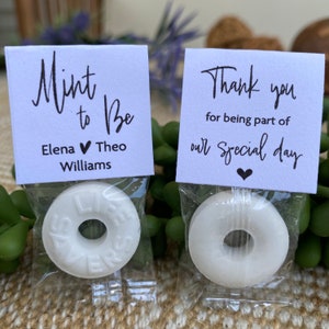 Puede incluir: Dos bolsas blancas de regalo con mentas blancas y tarjetas impresas. Una tarjeta dice "Mint to Be" con los nombres Elena y Theo Williams. La otra tarjeta dice "Gracias por ser parte de nuestro d&iacute;a especial".