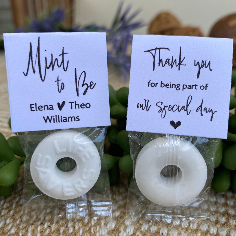 Puede incluir: Dos bolsas blancas de regalo con mentas blancas y tarjetas impresas. Una tarjeta dice "Mint to Be" con los nombres Elena y Theo Williams. La otra tarjeta dice "Gracias por ser parte de nuestro d&iacute;a especial".