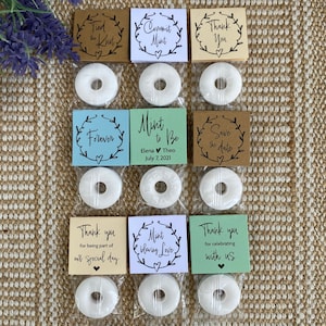 Puede incluir: Surtido de bolsas de regalo de boda con mentas blancas y tarjetas impresas. Las tarjetas tienen diferentes mensajes, que incluyen "Tied the Knot", "Commit Mint", "Thank You", "Forever", "Mint to Be", "Save the Date", "Thank you for being part of our special day", "Mint to be loving Love" y "Thank you for celebrating with us".
