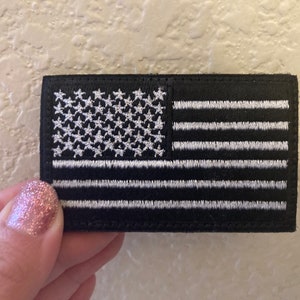 May include: A black embroidered patch with a white American flag design. The flag has 13 stripes and 50 stars.