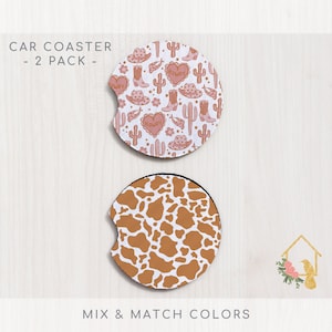 May include: Two car coasters, one with a pink and white pattern of cacti, boots, hats, and hearts with the word "Howdy" on the hearts, and the other with a brown and white cow print pattern.