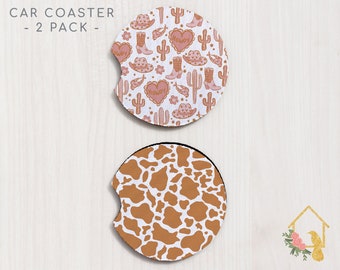 May include: Two car coasters, one with a pink and white pattern of cacti, boots, hats, and hearts with the word "Howdy" on the hearts, and the other with a brown and white cow print pattern.