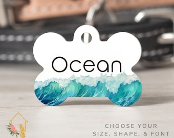 Pode incluir: Uma etiqueta para cão em forma de osso branca com um design de onda de oceano azul em aquarela e a palavra "Ocean" em texto preto.