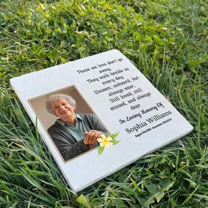 May include: A white ceramic memorial stone with a photo of a woman and a floral design. The stone has a quote about those we love don't go away, they walk beside us every day. The stone also includes the text "In Loving Memory Of Sophia Williams".
