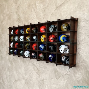 May include: A wooden wall-mounted display shelf with 36 compartments for storing miniature football helmets. The shelf is filled with helmets in various colours and team logos.