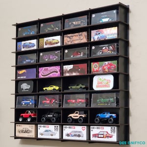 May include: A black wooden wall shelf with multiple clear acrylic display cases holding miniature toy cars. The shelf has 18 display cases and is filled with various makes and models of cars. The shelf is labeled "DESIGNIFYCO" at the bottom right corner.