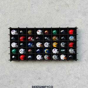 May include: A black wall shelf with 36 miniature football helmets in various team colours and logos. The helmets are arranged in a grid pattern.