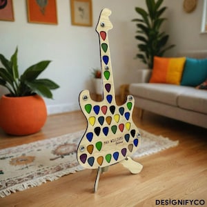 May include: A wooden guitar-shaped stand with a colourful assortment of guitar picks displayed on it. The stand is labelled "Max Williams Guitarist".
