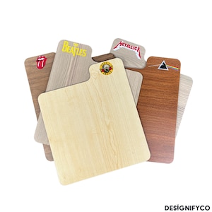 May include: A selection of wooden chopping boards, each bearing a different band logo. Logos include The Beatles, Metallica, and Guns N' Roses. The boards have a light wood grain finish and a handle, with a variety of shapes.