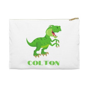 Puede incluir: Bolsa de lona blanca con cremallera con un dinosaurio verde de dibujos animados y el nombre "COLTON" en texto verde.