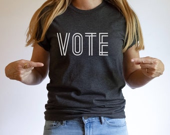 May include: A dark grey t-shirt with the word "VOTE" printed in white on the front. The letters are outlined in white.