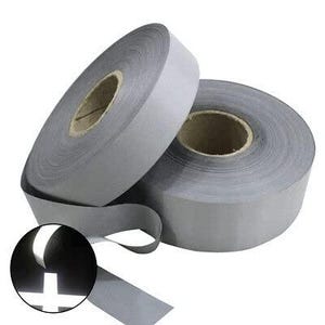 May include: Two rolls of reflective silver tape are displayed, one partially unrolled. A close-up shows the tape's reflective properties, with a bright white cross shape illuminated. The tape is designed for enhanced visibility.