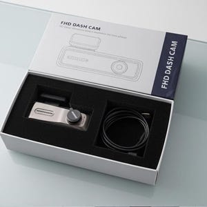 May include: An open white box containing a silver dash cam, a black cable, and a small black component. The box is labeled "FHD DASH CAM" in black text. The dash cam has a silver body and a black dial.