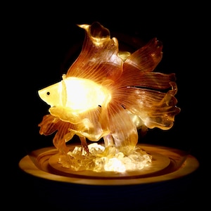 May include: A glowing, translucent orange fish sculpture with a light inside, sitting on a white base with clear crystals.