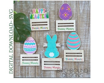 May include: A set of six wooden Easter bunny money holders. Each holder features a different design, including a bunny, an egg, and a sign that says "Happy Easter". The holders are painted in pastel colors and have the words "Bunny Money" written on them.