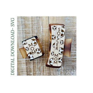 以下が含まれることがあります： 白地に黒のサッカーボールが描かれた、茶色のヘアクリップ2つ。大きい方のクリップには「Soccer Mom」と印刷されています。小さい方のクリップには「MOM」と印刷されています。