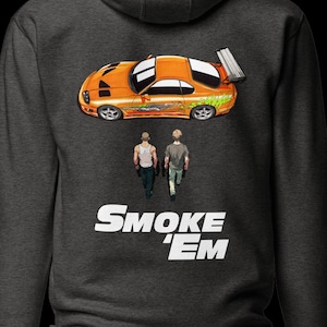 May include: Dark gray hoodie featuring an orange sports car graphic with a rear wing and the text "Smoke 'Em". Two figures are walking below the car. The car has green and white accents.