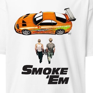 May include: White t-shirt featuring an orange sports car graphic with green and silver accents, and two figures walking away. The text "SMOKE 'EM" is printed in black below the figures.