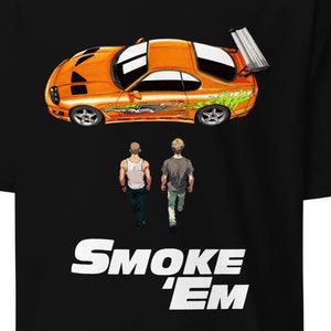 May include: Black t-shirt featuring an orange sports car graphic with green and white accents, and two figures walking away. The text "SMOKE 'EM" is printed in white.