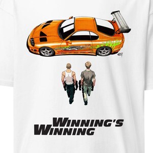 May include: White t-shirt featuring an orange sports car graphic with a rear spoiler and green accents. Below the car are two figures walking away, with the text "WINNING'S WINNING" in bold black letters.