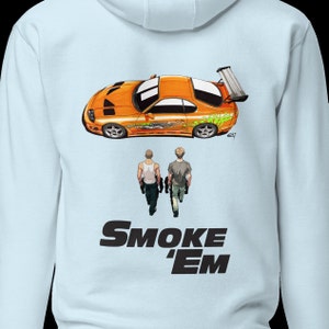 May include: Light blue hoodie featuring an orange sports car graphic with green accents and two figures walking. The text "SMOKE 'EM" is printed in black below the figures. The hoodie is made of a soft material.