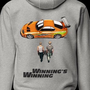 May include: A gray hoodie featuring an orange sports car graphic with green and white accents. Below the car are two figures walking away, and the text "Winning's Winning" is printed at the bottom. The hoodie has a hood and a front pocket.