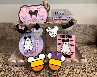 May include: A tiered wooden tray decorated with Halloween-themed wooden ornaments. The ornaments feature Mickey Mouse characters, ghosts, and candy corn. The tray also includes signs that say "Trick or Treat", "Main Street", "Happy Halloween", and "Tis the Season".