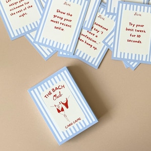 May include: A card game called "The Bach Club" with a light blue and white striped design. The card game features a red bikini graphic and the words "CARD GAME". Individual cards with "Dare" prompts are scattered around, including "Try your best twerk for 10 seconds."