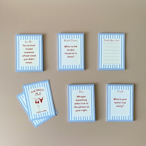 May include: A set of blue and white striped cards with red text, designed for a game. The cards feature prompts such as "What is the bride's favourite TV show?" and "Whisper something seductive to the person on your right."