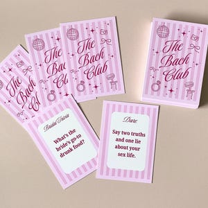 Pode incluir: Conjunto de jogos para festas rosa e branco com o texto "The Bach Club" na caixa e nos cart&otilde;es. Os cart&otilde;es apresentam um fundo listrado, uma bola de discoteca, um anel e outros gr&aacute;ficos. Alguns cart&otilde;es t&ecirc;m perguntas.