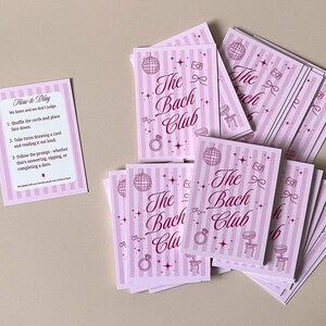 Pode incluir: Um conjunto de cart&otilde;es rosa e branco listrados com o texto "The Bach Club" em it&aacute;lico. Os cart&otilde;es apresentam ilustra&ccedil;&otilde;es de uma bola de discoteca, um anel, uma c&acirc;mera e uma cadeira. Um cart&atilde;o menor com instru&ccedil;&otilde;es tamb&eacute;m est&aacute; presente.