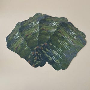 May include: A set of four scalloped-edge menu cards featuring a dark green and blue impressionist-style floral print. Each card displays the word Menu in white script at the top, followed by a printed list of food courses in white text.