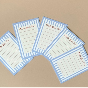 May include: Five rectangular cards with a light blue striped border and the words "Create Your Own" in red script. Each card has a cream-coloured interior with dashed lines for writing.