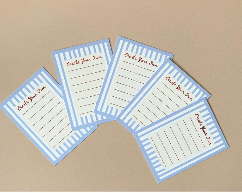 May include: Five rectangular cards with a light blue striped border and the words "Create Your Own" in red script. Each card has a cream-coloured interior with dashed lines for writing.
