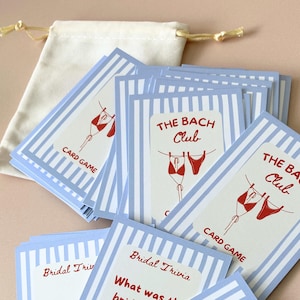May include: A collection of bridal trivia cards featuring blue and white striped borders and red bikini illustrations. The cards are labelled "THE BACH Club" and "CARD GAME". A small drawstring bag is also included.