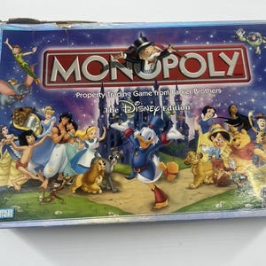 May include: A rectangular Monopoly The Disney Edition board game box featuring the Monopoly logo, Rich Uncle Pennybags, and various Disney characters including Donald Duck, Peter Pan, and Simba against a dark blue castle background.