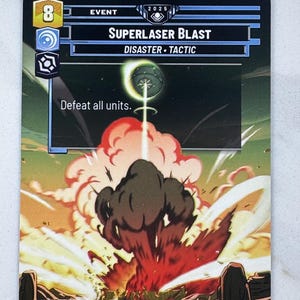 May include: A trading card featuring the text "SUPERLASER BLAST" and "DISASTER • TACTIC." The card depicts an explosion with a green energy beam. The card has a black border and the text "Defeat all units."