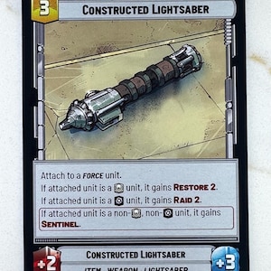 May include: A trading card featuring a Constructed Lightsaber. The card has a black border with the text "UPGRADE" at the top. The lightsaber is depicted in shades of silver, brown, and green. The card includes game text and stats.