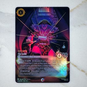 May include: A trading card featuring Goliath, a Clan Leader, with a purple and red color scheme. The card includes the text "Dusk to Dawn" and "Stone by Day", along with the card's number and a Disney Lorcana logo.