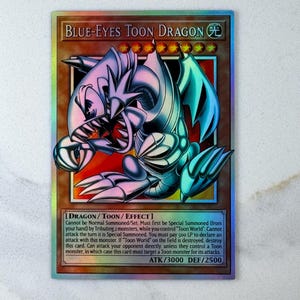 Puede incluir: Una tarjeta coleccionable holográfica con el Dragón Toon de Ojos Azules. La tarjeta tiene un borde marrón y presenta un dragón de dibujos animados en tonos azules, blancos y turquesas. El texto incluye el nombre del monstruo, sus atributos y estadísticas de ataque/defensa.