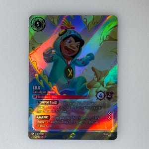 Op de afbeelding: Een holografische ruilkaart met Lilo uit Disney's Lilo & Stitch. Lilo is afgebeeld in een teal onesie met een gele 'X'. De kaart heeft een regenboogfolie-effect en bevat speltekst en karakterstatistieken.