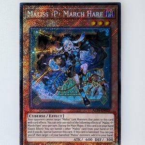 May include: A trading card for the "Maliss (P) March Hare" monster from the Yu-Gi-Oh! Trading Card Game. The card is a dark cyberse monster with an attack power of 600 and a defense power of 300. The card features an illustration of a young woman with white hair and a blue dress, holding a staff with a heart-shaped top. The card text describes the monster's abilities, which include targeting "Maliss" Link Monsters and summoning itself from the hand.