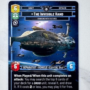 May include: A trading card featuring a large spaceship, "The Invisible Hand," with a dark blue and gray color scheme. The card includes text and symbols, with a space background and several smaller ships.