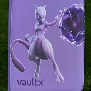 May include: A light purple rectangular trading card binder featuring a graphic of the character Mewtwo casting a dark purple energy sphere. The brand name vaultx is printed in the bottom left corner in a dark purple sans-serif font.